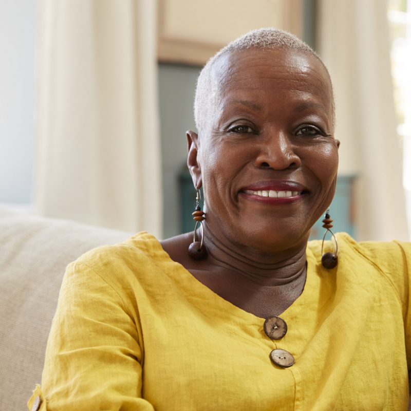 Portrait Of Smiling Senior Woman Sitting On Sofa At Home senior woman smiling on a couch