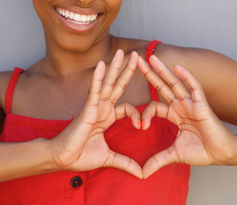 Close up young woman smiling with heart shape hand sign Close up portrait of young woman smiling with heart shape hand